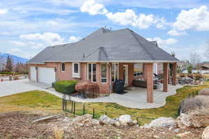 Rear view of property featuring an attached garage, brick siding, a patio area, a mountain view, and roof with shingles