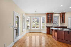 Kitchen featuring glass fronted cabinets, dark stone counters, light wood-type flooring, a chandelier, and stainless steel appliances