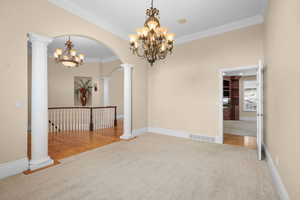 Empty room with decorative columns, light carpet, crown molding, arched walkways, and hanging lights