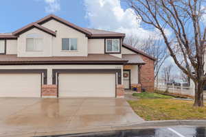 Traditional townhome featuring brick siding, stucco siding, driveway, and a garage