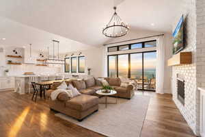 Living room with wood-type flooring, a fireplace, suspended lighting, and vaulted ceiling