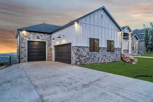 View of front of property with board and batten siding, a garage, stone siding, and driveway