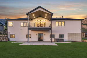 Back of property at dusk with a hot tub, a patio area, a lawn, and stucco siding
