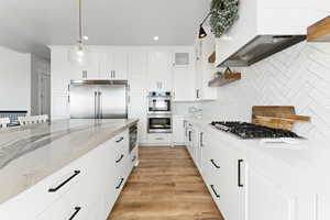 Kitchen with light stone countertops, built in appliances, white cabinetry, open shelves, and light wood-style floors