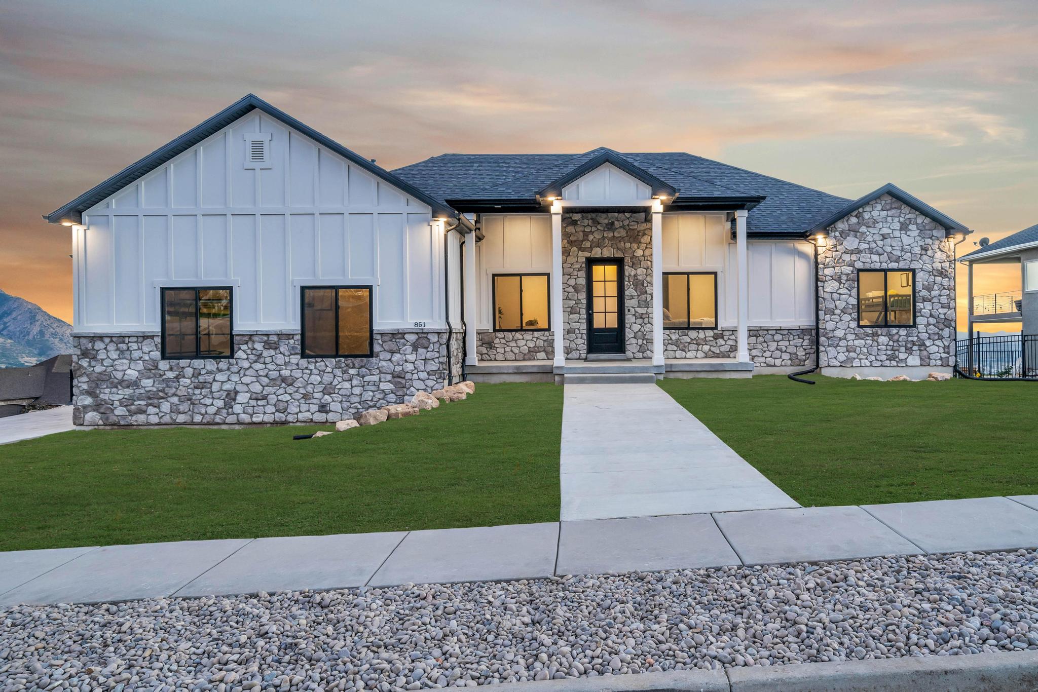 Modern farmhouse style home with board and batten siding, covered porch, a lawn, stone siding, and roof with shingles