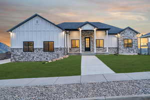 Modern farmhouse style home with board and batten siding, covered porch, a lawn, stone siding, and roof with shingles