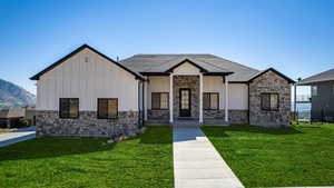 Modern inspired farmhouse with board and batten siding, stone siding, covered porch, and a front yard
