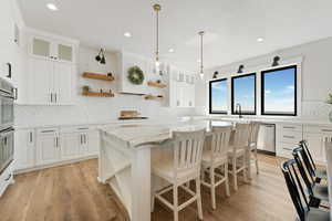 Kitchen with glass insert cabinets, light stone counters, and white cabinets