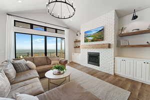 Living area with a brick fireplace, wood finished floors, lofted ceiling, and a chandelier