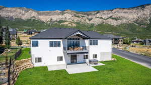 Rear view of house with a balcony, a yard, stucco siding, a mountain view, and a patio