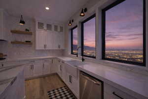 Kitchen featuring white cabinets, stainless steel dishwasher, glass insert cabinets, light wood-style floors, and open shelves