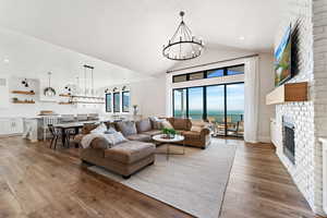 Living room featuring hardwood / wood-style floors, a chandelier, a brick fireplace, and vaulted ceiling