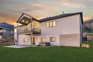 Back of house at dusk with a patio area, a hot tub, and stucco siding