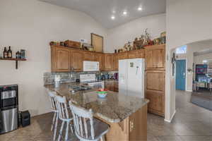 Kitchen featuring a breakfast bar area, wood finish cabinetry, backsplash, white appliances, and arched walkways