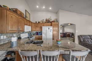 Kitchen featuring a kitchen bar, white appliances, vaulted ceiling, light stone counters, and wood finish cabinetry
