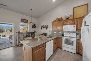 Kitchen with white appliances, a peninsula, vaulted ceiling, wood finish cabinetry, and light stone counters