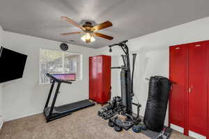 Exercise area with light carpet, a ceiling fan, and a textured ceiling