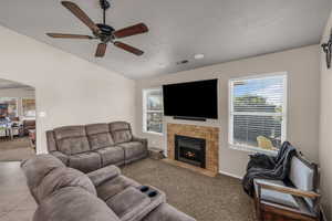 Carpeted living room featuring plenty of natural light, a ceiling fan, arched walkways, and a fireplace with flush hearth