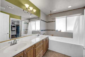 Full bath with shower / tub combo with curtain, double vanity, a textured ceiling, a spacious closet, and a chandelier