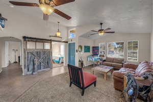 Tiled living area with a barn door, a ceiling fan, arched walkways, and a high textured ceiling