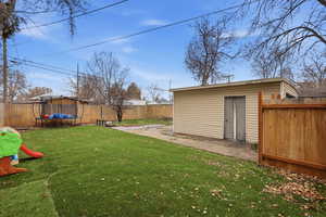 Fenced backyard featuring a patio, a trampoline, and an outbuilding