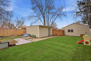 Fenced backyard featuring a gate, a patio area, and an outbuilding