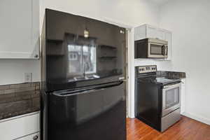 Kitchen featuring stainless steel appliances, dark wood-style floors, white cabinets, and dark stone counters