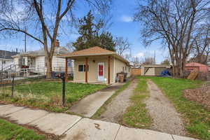 Bungalow-style home featuring an outbuilding, a shingled roof, a detached garage, a chimney, and driveway