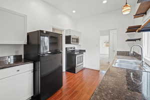 Kitchen featuring stainless steel appliances, dark stone counters, open shelves, wood tiled floors, and white cabinetry
