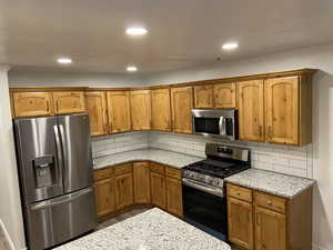 Kitchen with stainless steel appliances, backsplash, light stone counters, wood finish cabinetry, and recessed lighting
