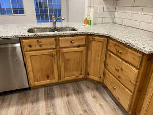 Kitchen with stainless steel dishwasher, light stone countertops, wood finished floors, and backsplash