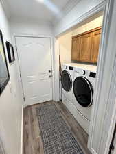 Laundry room featuring dark wood-type flooring, cabinet space, washing machine and clothes dryer, and ornamental molding