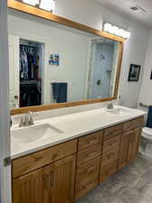 Full bathroom featuring double vanity, a spacious closet, tiled shower, and stone finish floors