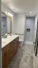 Bathroom with double vanity, a shower stall, dark stone finish flooring, and a textured ceiling