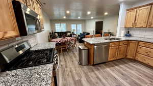 Kitchen featuring backsplash, stainless steel appliances, light stone counters, open floor plan, and a peninsula