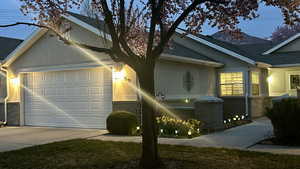 View of front of home with stucco siding, an attached garage, roof with shingles, driveway, and stone siding