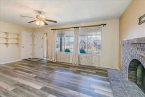 Unfurnished living room featuring a ceiling fan, dark wood-style flooring, and a fireplace