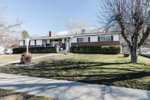 Ranch-style home with brick siding, covered porch, a front lawn, and a chimney