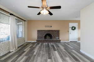 Unfurnished living room with ceiling fan, dark wood finished floors, and a brick fireplace
