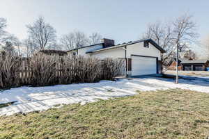 View of home's exterior featuring a garage, a chimney, brick siding, a lawn, and driveway