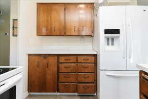Kitchen featuring white refrigerator with ice dispenser, light countertops, wood finish cabinetry, and black electric range oven