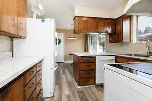Kitchen with white appliances, light countertops, a peninsula, light wood-type flooring, and decorative light fixtures