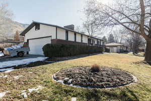View of property exterior with a chimney, brick siding, an attached garage, a lawn, and a mountain view