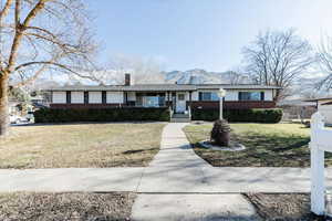 Ranch-style home featuring a front yard, covered porch, a chimney, and brick siding