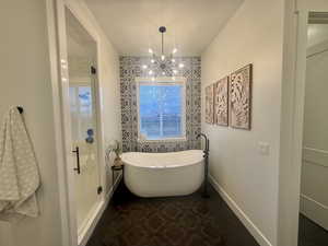 Bathroom with dark tile patterned floors, a shower stall, a soaking tub, and suspended lighting