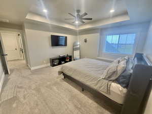 Bedroom with a tray ceiling, light colored carpet, ceiling fan, and recessed lighting