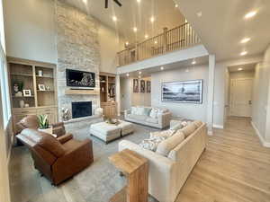 Living area with a high ceiling, a stone fireplace, light wood-style flooring, built in shelves, and recessed lighting
