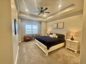 Carpeted bedroom featuring a raised ceiling, ceiling fan, and recessed lighting