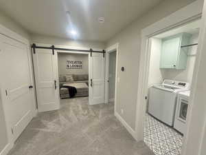 Laundry room with light colored carpet, washing machine and clothes dryer, a barn door, and cabinet space