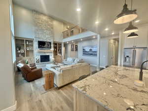Living area featuring a high ceiling, light wood-type flooring, a fireplace, built in shelves, and recessed lighting
